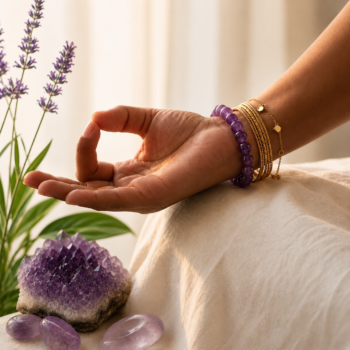 Woman wearing a purple Amethyst Crystal Bracelet with gold bangles beside an Amethyst cluster and lavender in a peaceful setting.
