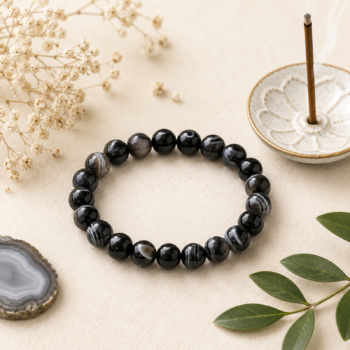 Suleimani Hakik Black Agate crystal bracelet with natural black, gray and white banded beads on a cream background