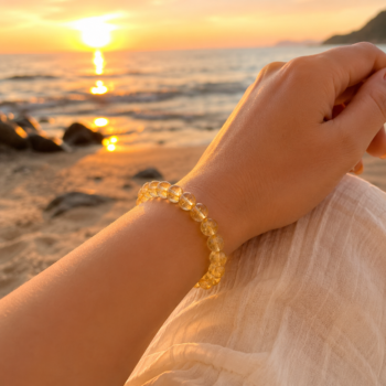 Woman wearing a golden Citrine crystal bracelet on her wrist at the beach during sunset