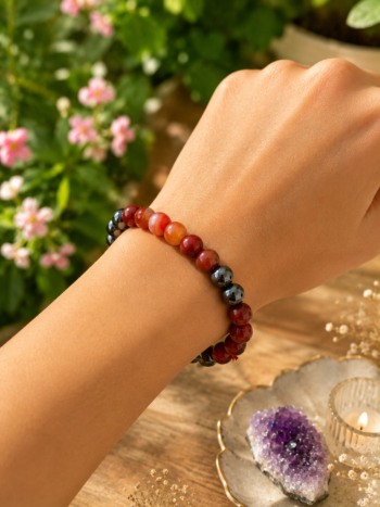Woman wearing the Mesh Rashi Bracelet by Mesmera World featuring Black Onyx, Carnelian, and Red Jasper crystals in a natural garden setting.