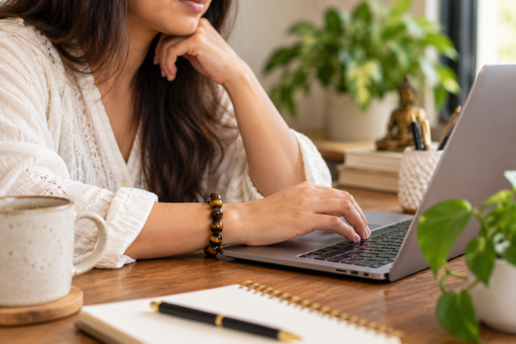 Woman wearing a Tiger Eye crystal bracelet while working at a laptop desk
